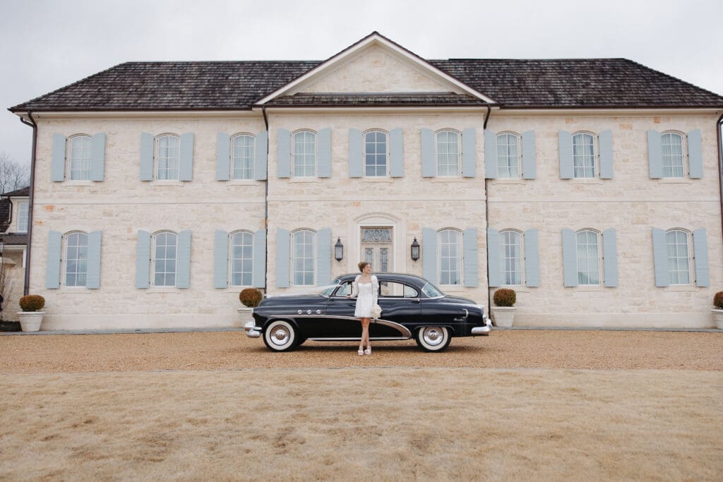 Bride posing with a vintage black car in front of The Conservatory at Crosswicks wedding venue in Trussville Alabama