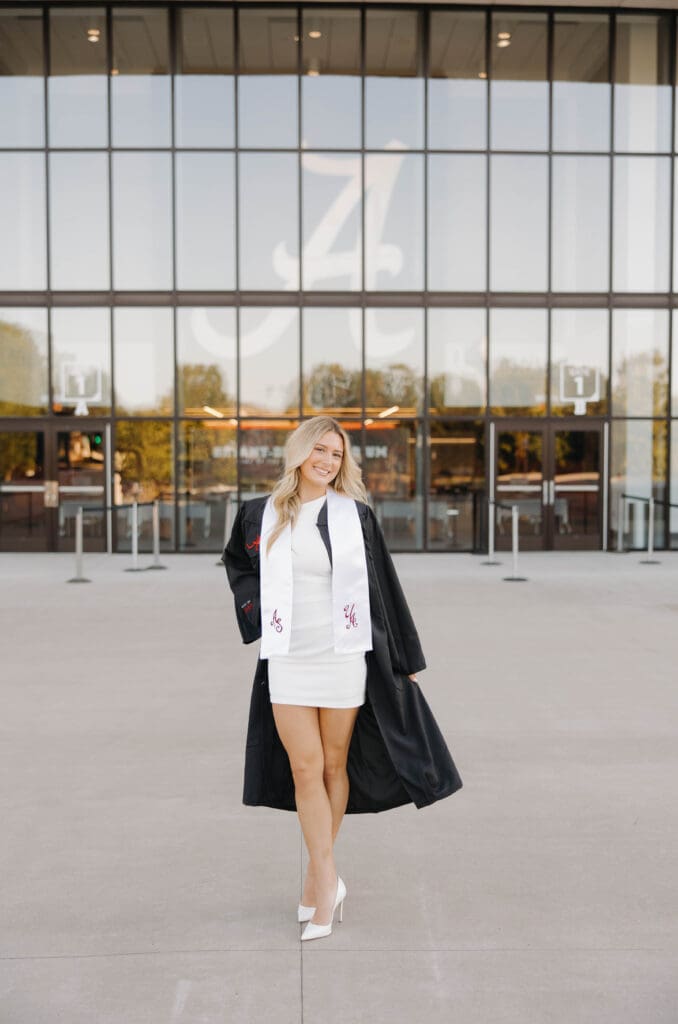 University of Alabama graduate in cap and gown standing in front of Bryant-Denny Stadium entrance in Tuscaloosa Alabama