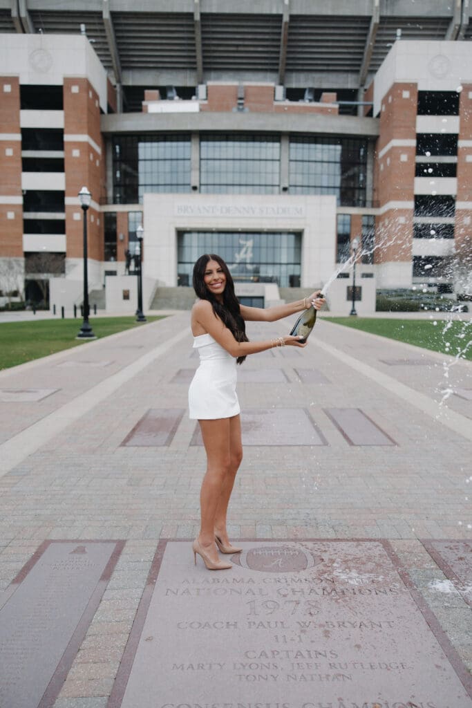 University of Alabama graduate popping champagne in front of Bryant-Denny Stadium in Tuscaloosa Alabama during senior photos