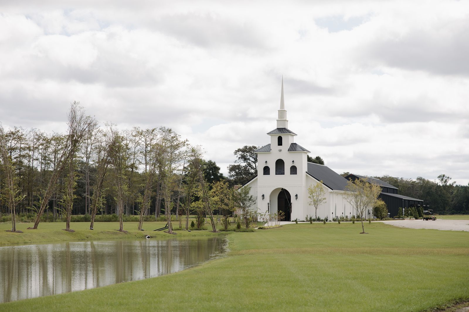 Exterior of Chapel in the Field wedding venue in Bonifay, Florida, featuring a white chapel, pond, and green lawn beneath a cloudy sky.